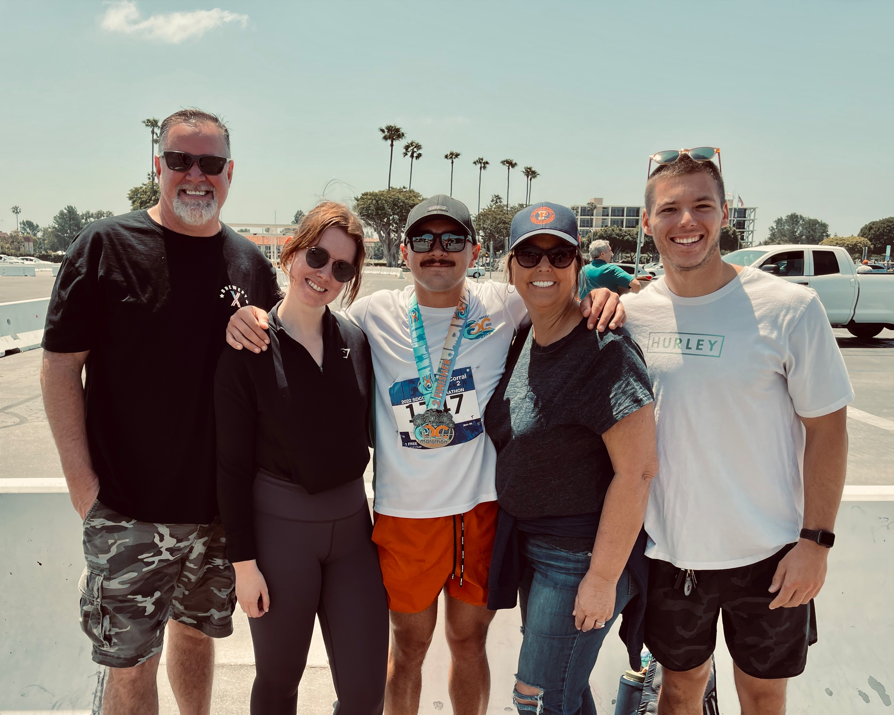Five people stand in a parking lot, one holds a metal from completing a marathon